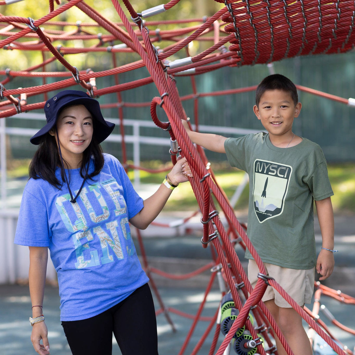 Adult woman wearing blue Queens graphic Tshirt with transit map standing outside