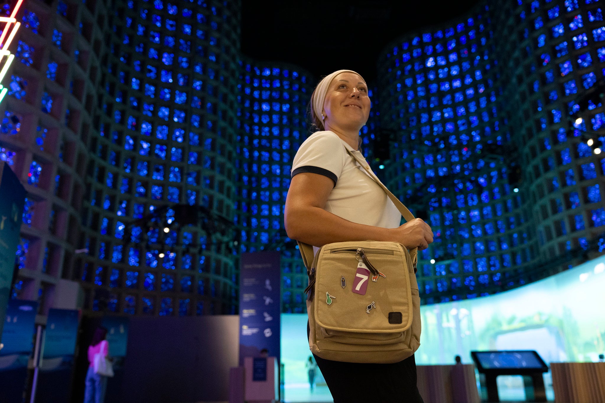 Woman carrying a beige shoulder bag inside the museum with blue lit up walls behind her