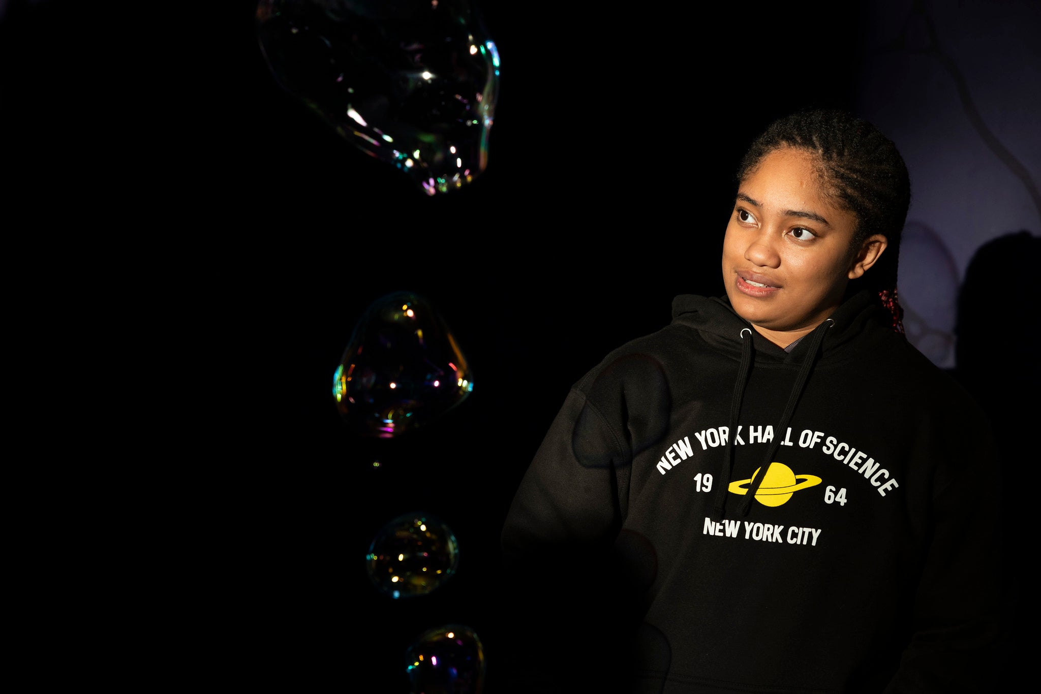 Woman wearing black NYSCI branded sweatshirt with yellow Saturn graphic at a display in the museum