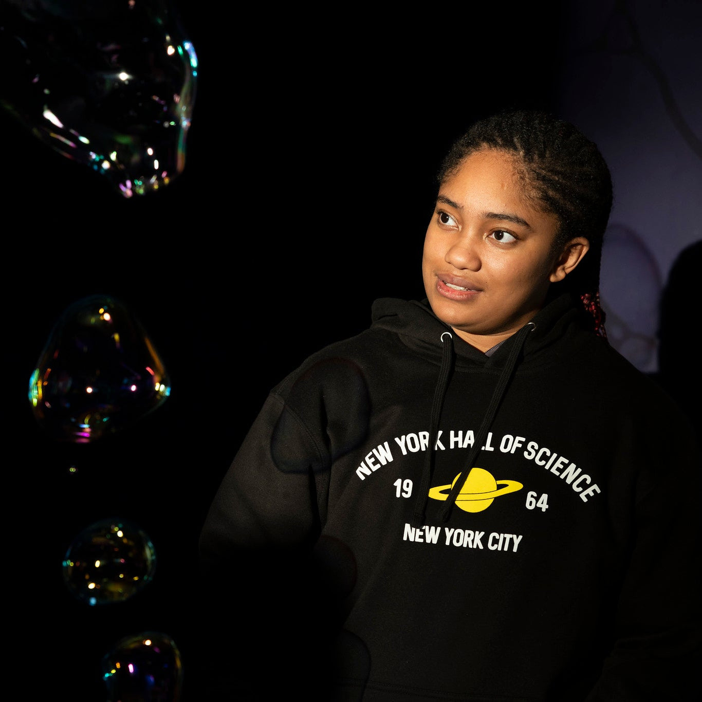 Woman wearing black NYSCI branded sweatshirt with yellow Saturn graphic at a display in the museum