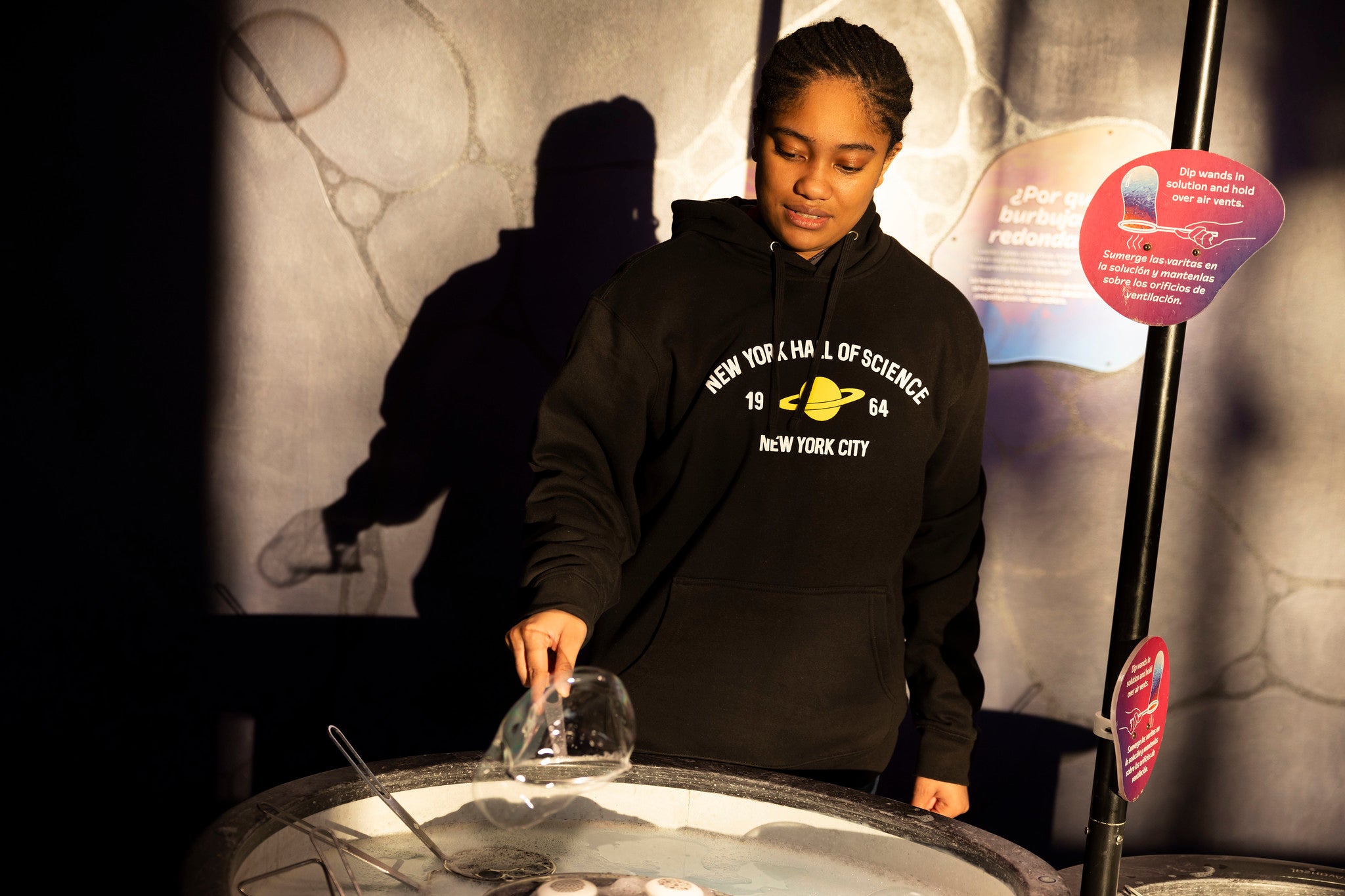 Woman wearing black NYSCI branded sweatshirt with yellow Saturn graphic at a display in the museum