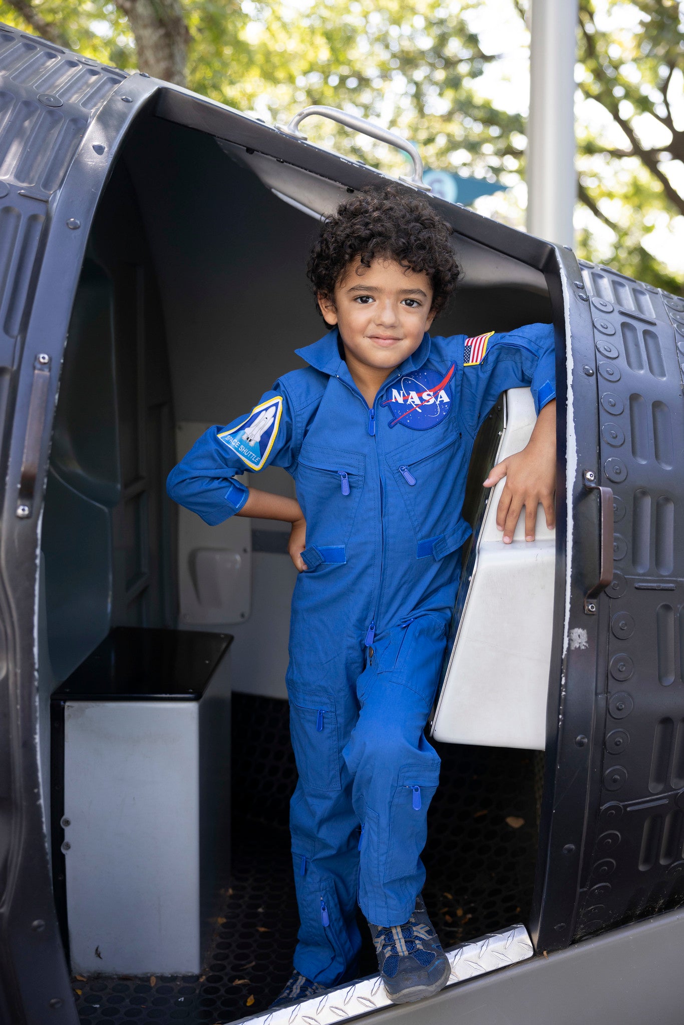 boy wearing blue NASA jumpsuit inside a black NASA capsule in the park