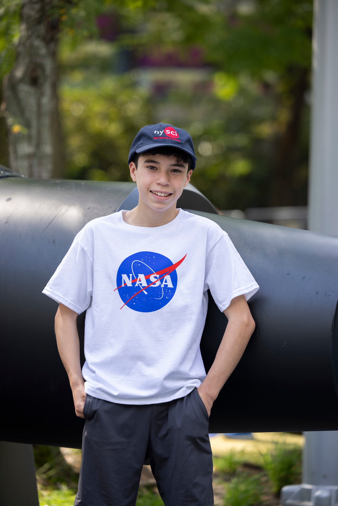 Child posing wearing white NASA t-shirt and nysci baseball cap outside