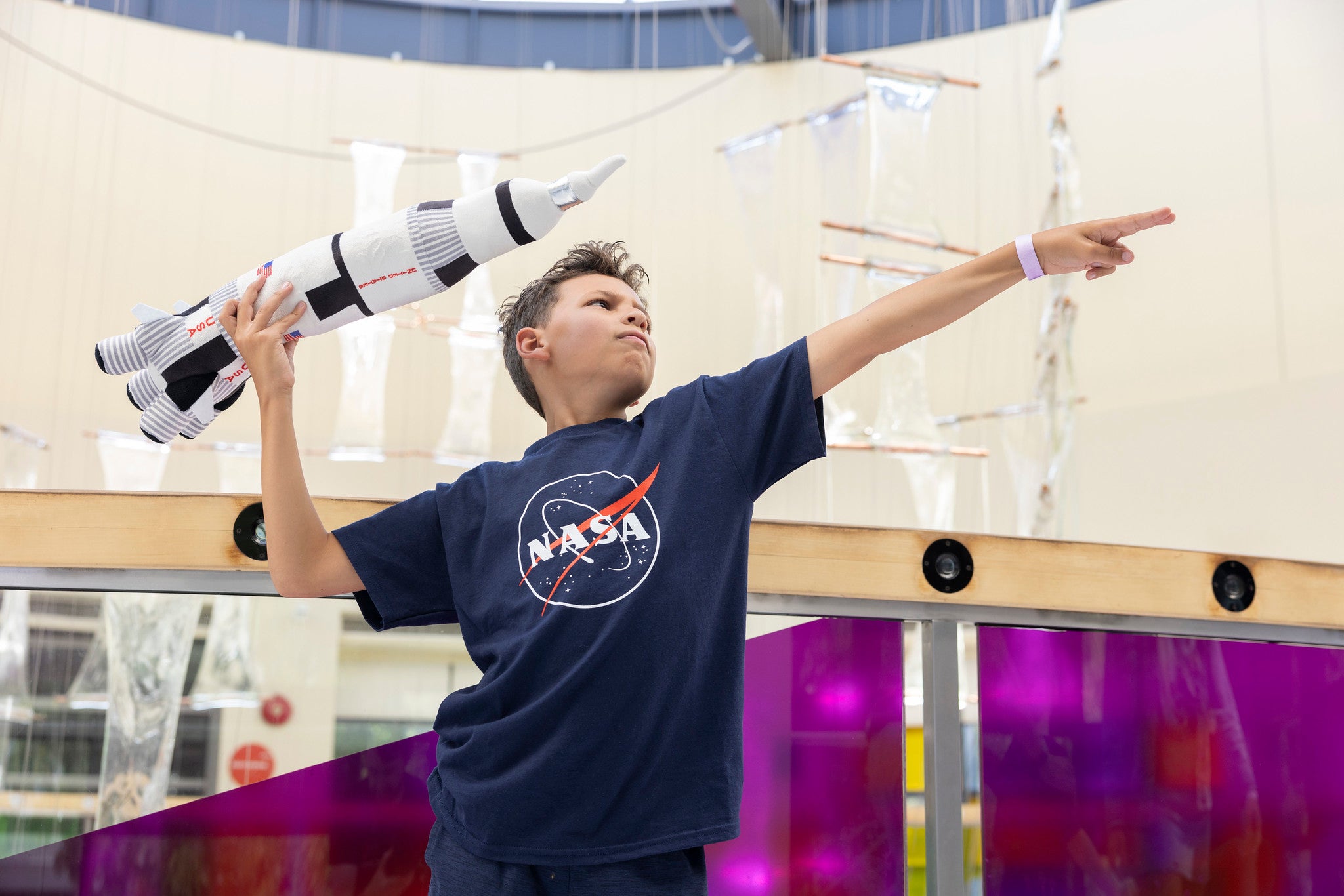 boy doing superman pose with plush NSA rocket wearing a blue NASA logo t-shirt