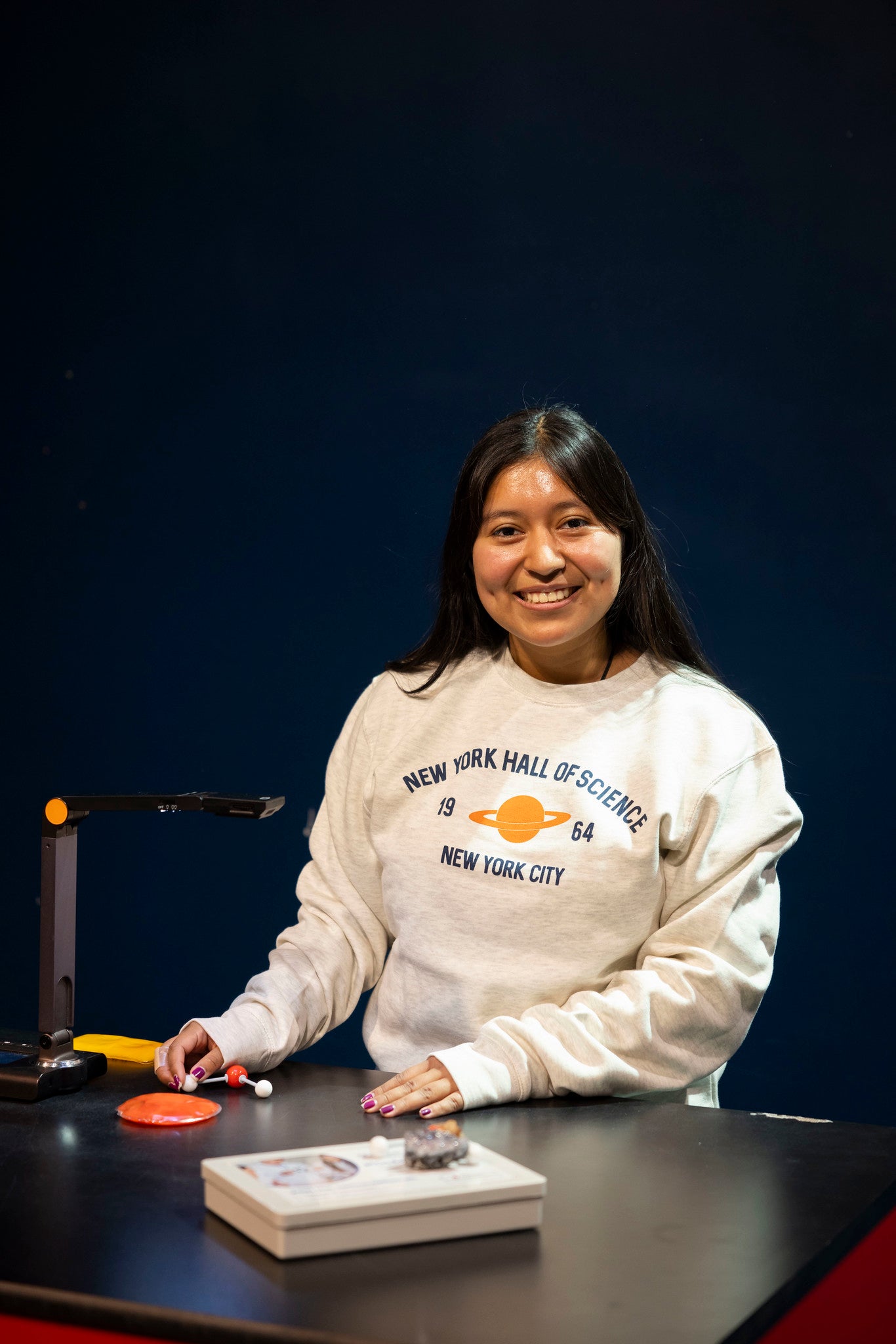Beige sweatshirt on a girl in a science lab with words NY Hall of Science, NYC 1964 and a graphic of Saturn