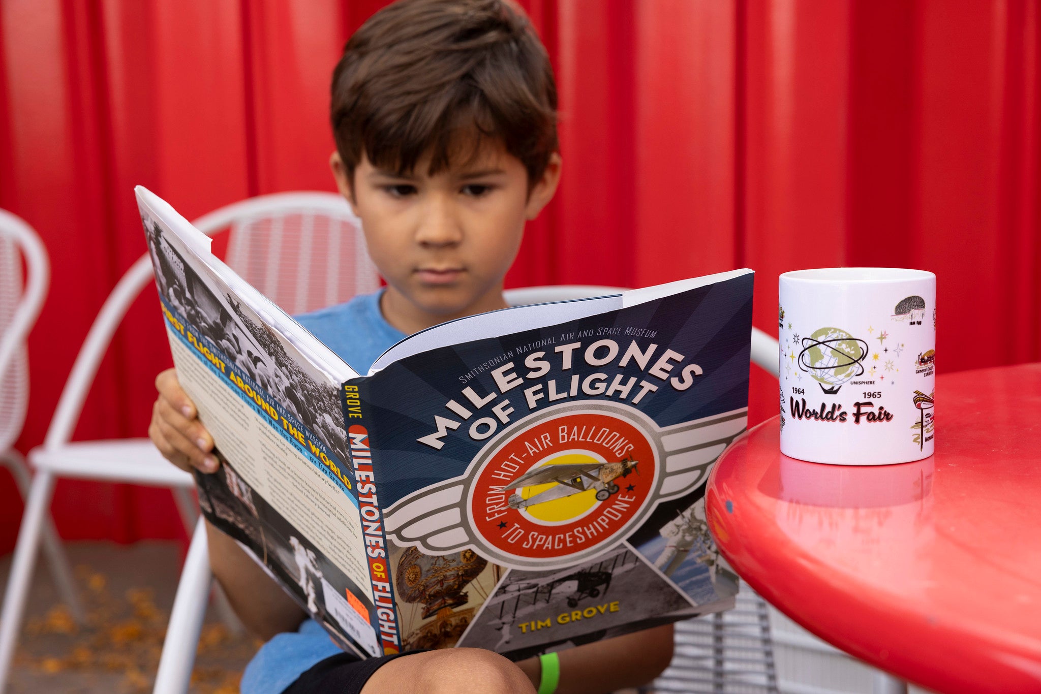 Child boy reading the book Milestones of Flight at a red table