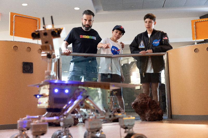 three people looking over the display for the Merse rover wearing nysci and NASA branded t-shirts