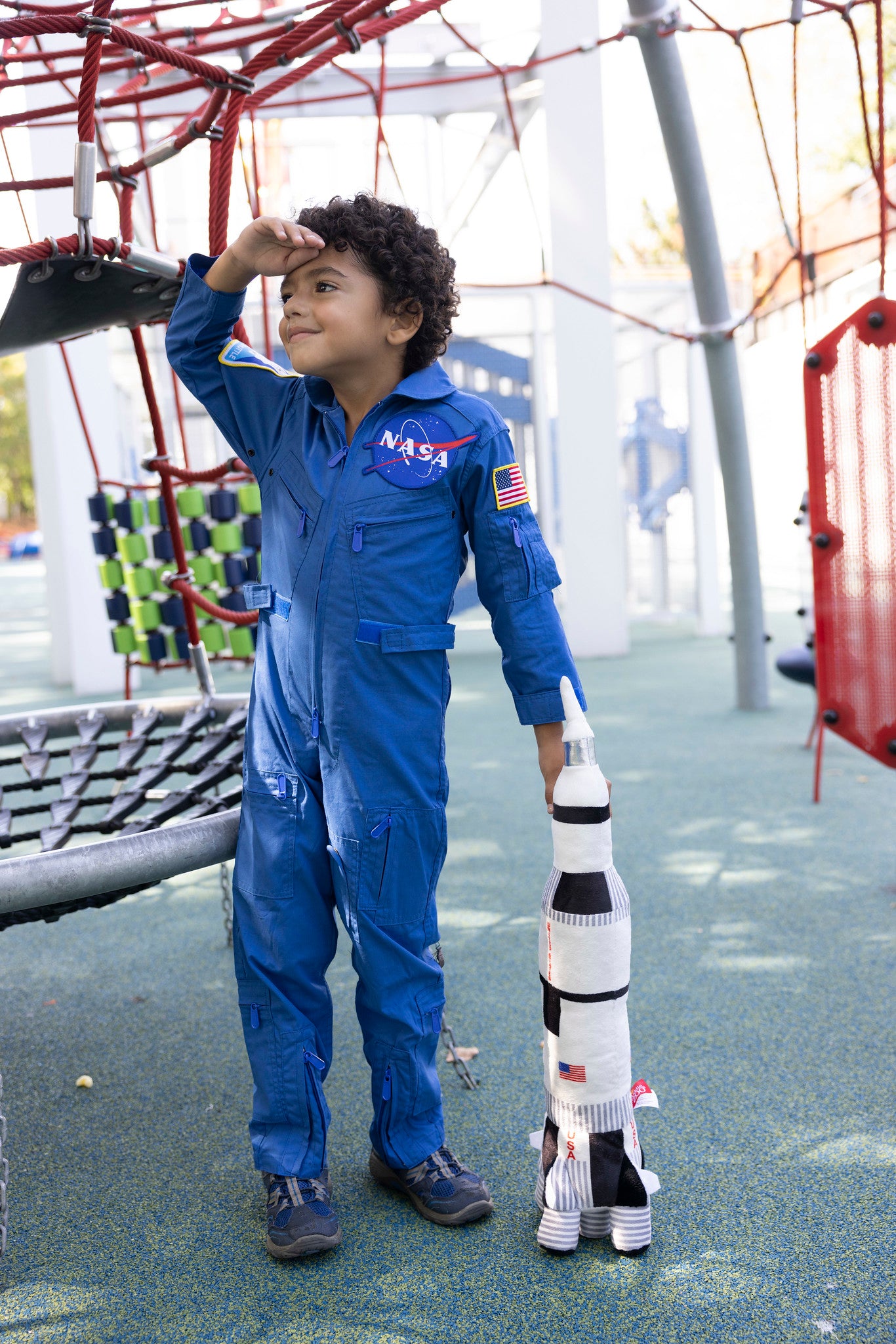 Child in blue jump suit playing in a park with a plush toy spaceship