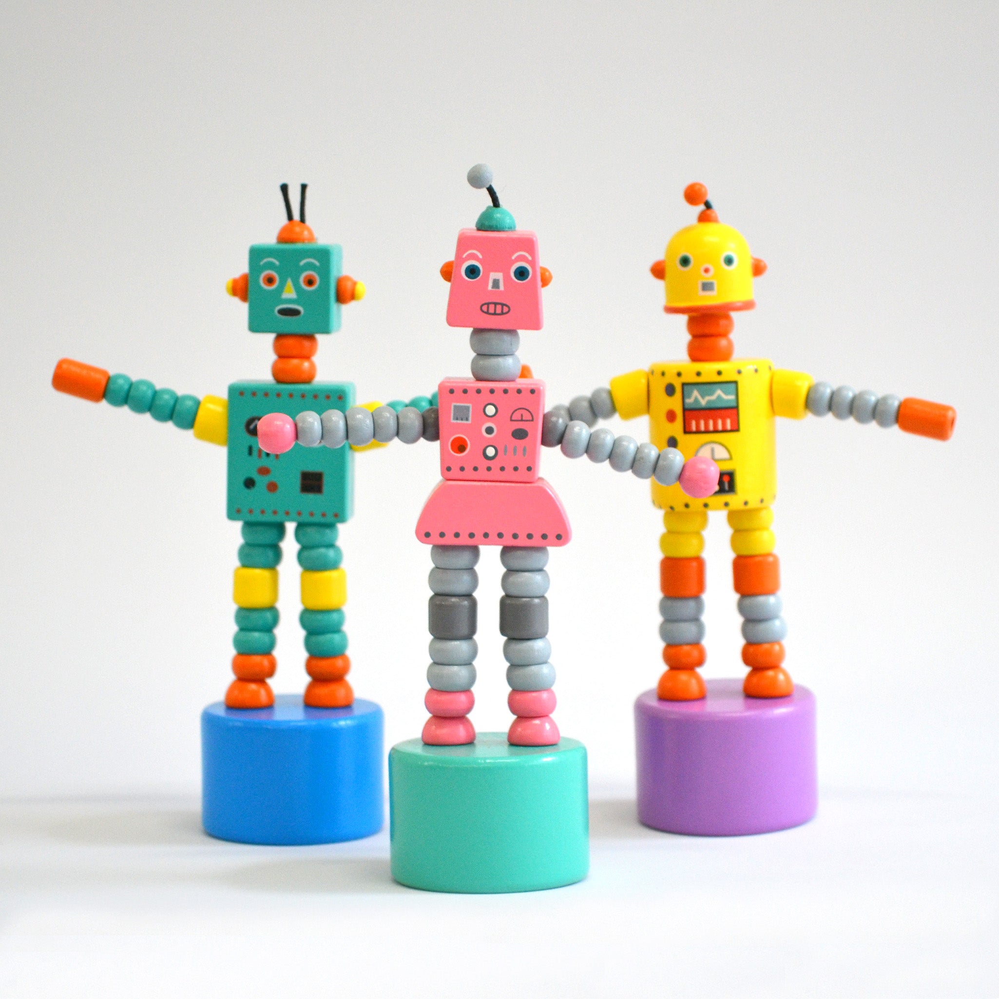 Three toy robots in green, pink and yellow