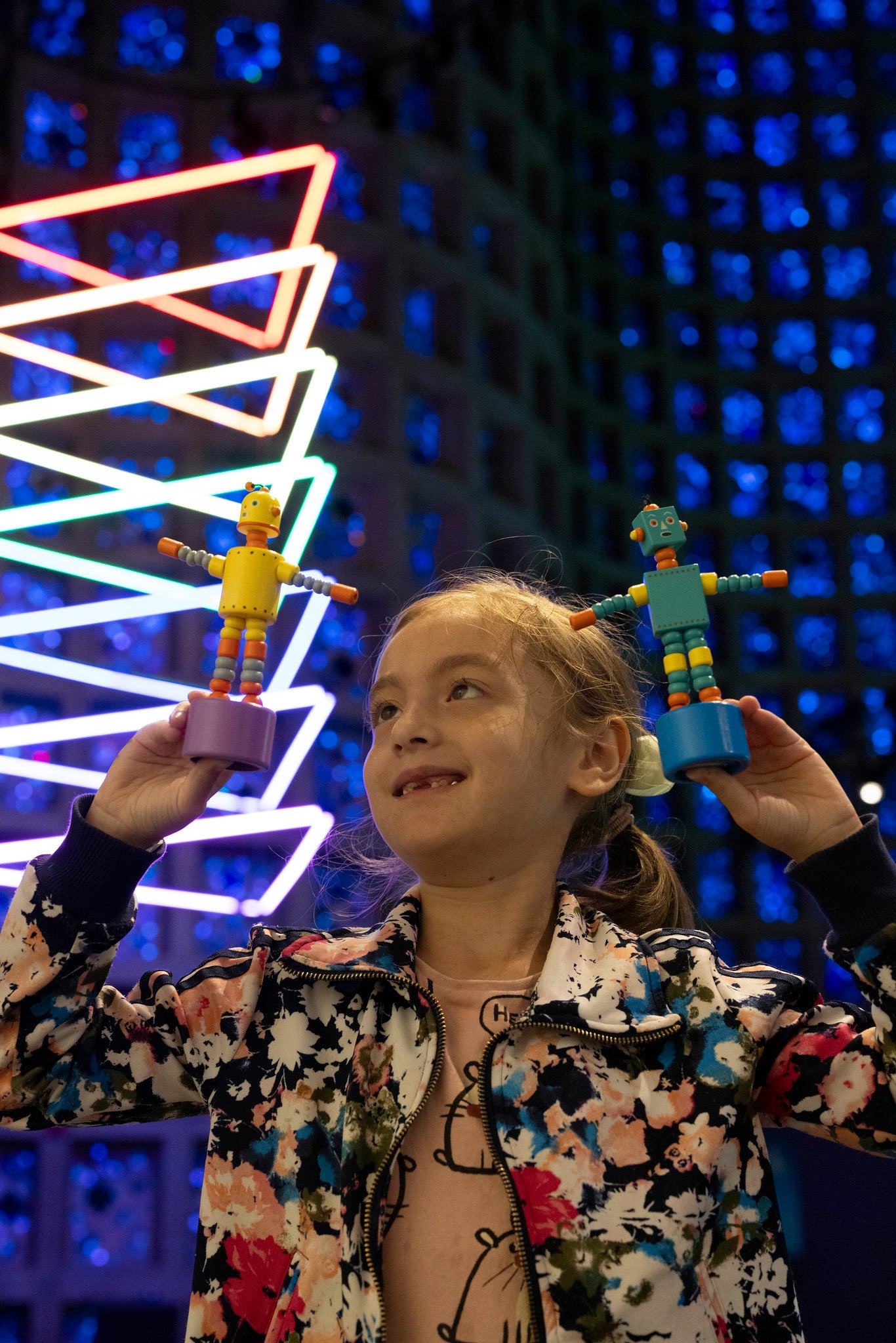 Girl smiling and holding up two plastic robots