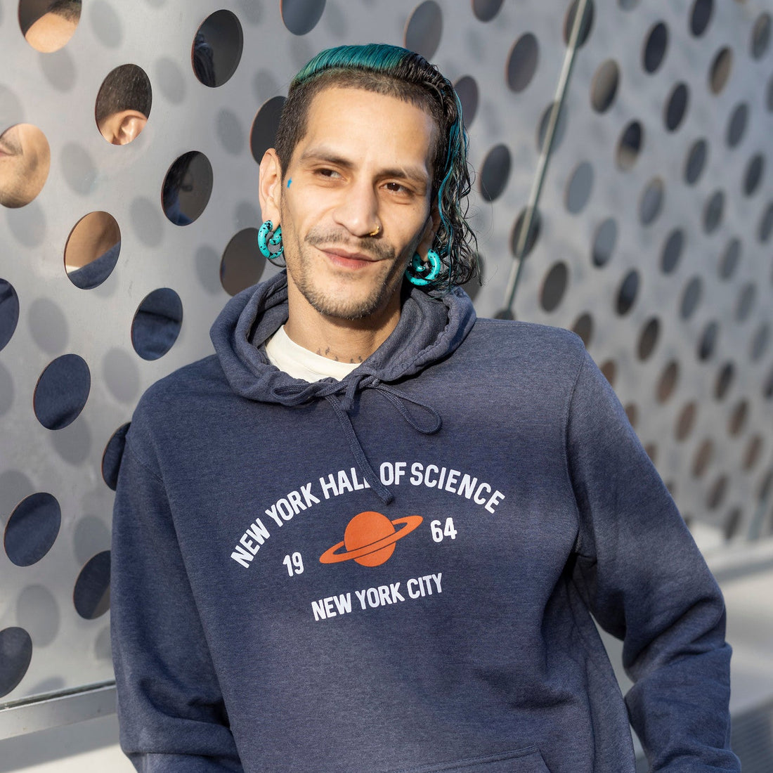 Man wearing a blue hoodie with a science museum logo against a textured wall.