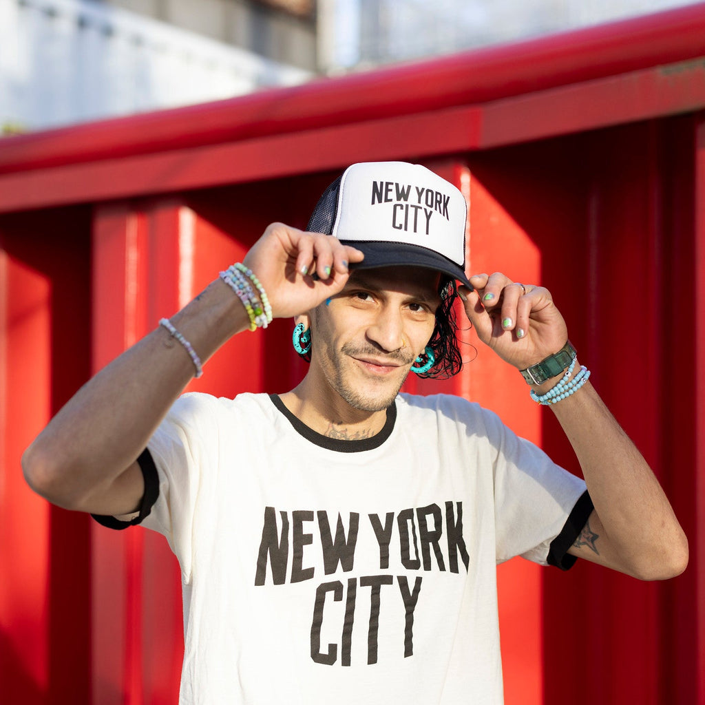 Person wearing a 'New York City' cap and t-shirt in front of a red background