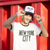 Man wearing a 'New York City' t-shirt and cap against a red background