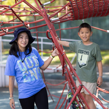 Adult woman wearing blue Queens graphic Tshirt with transit map standing outside