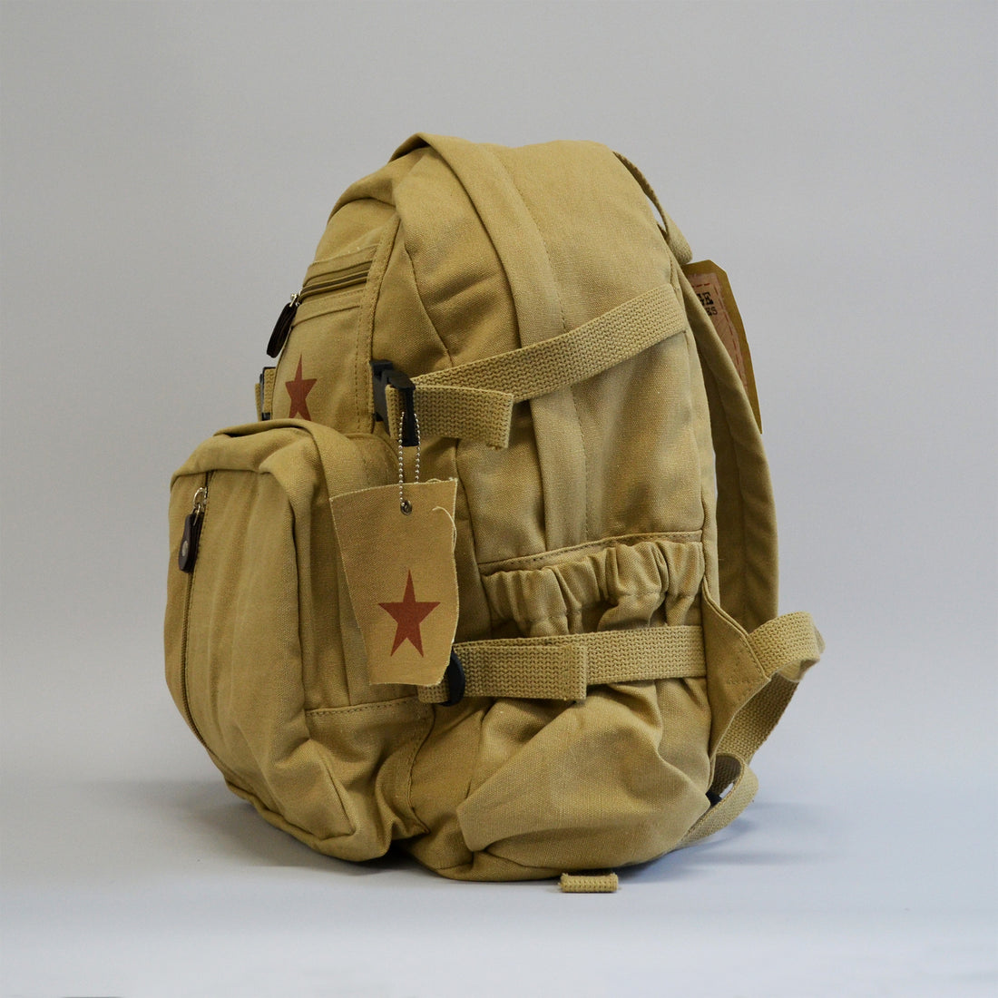 Khaki colored backpack with a buckle, a water bottle holder, a tag with a star facing the left side