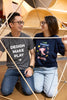 A couple looking at each other. The male has a t-shirt which is gray and says DESIGN MAKE PLAY on it, while the woman has a t-shirt which says I like science a'lotl.