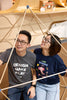 Man and woman inside wooden triangle display wearing DESIGN - MAKE - PLAY and "I like science" t-shirts