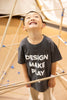 boy smiling and looking up standing in a museum display wearing a design-make-play grey t-shirt