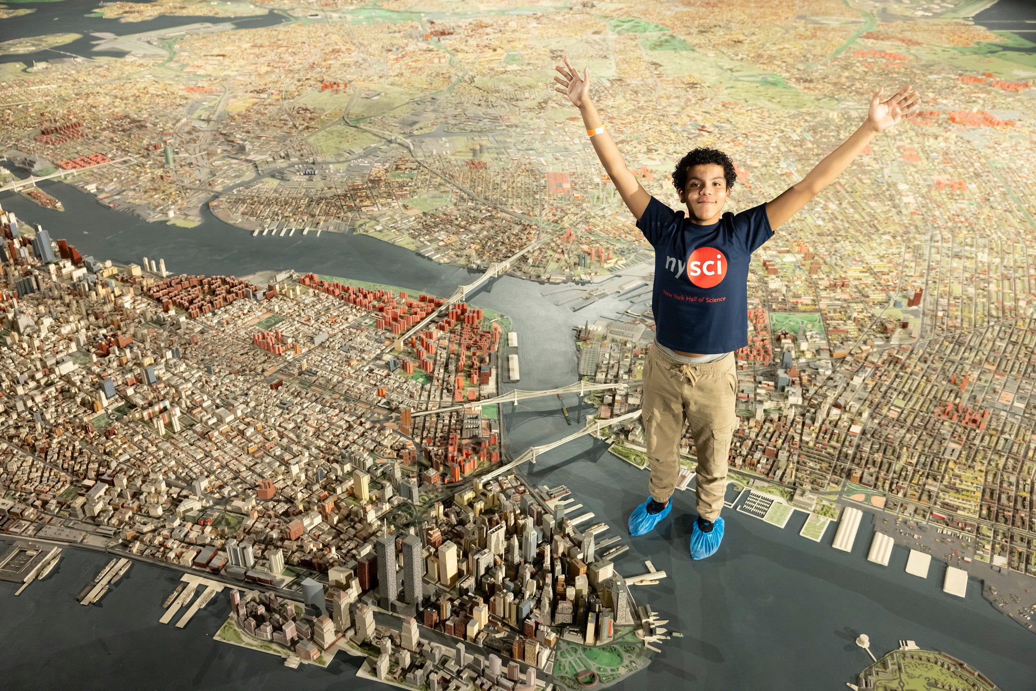 Child wearing a nysci blue t-shirt standing in the scale model of new york city