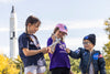 three children playing with a silver astronaut toy wearing NASA branded clothes
