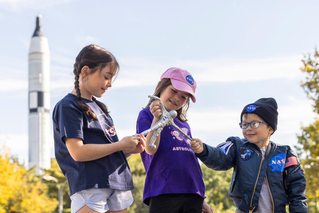 three children playing with a silver astronaut toy wearing NASA branded clothes