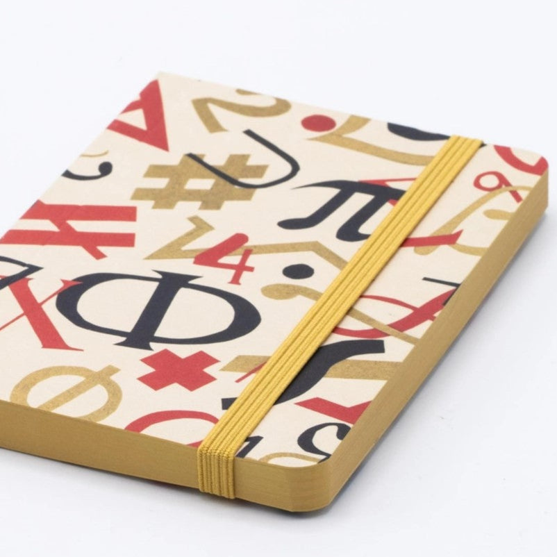 Colorful cover of notebook with math symbols in red, gold and black on a beige background - notebook laying flat on white table surface