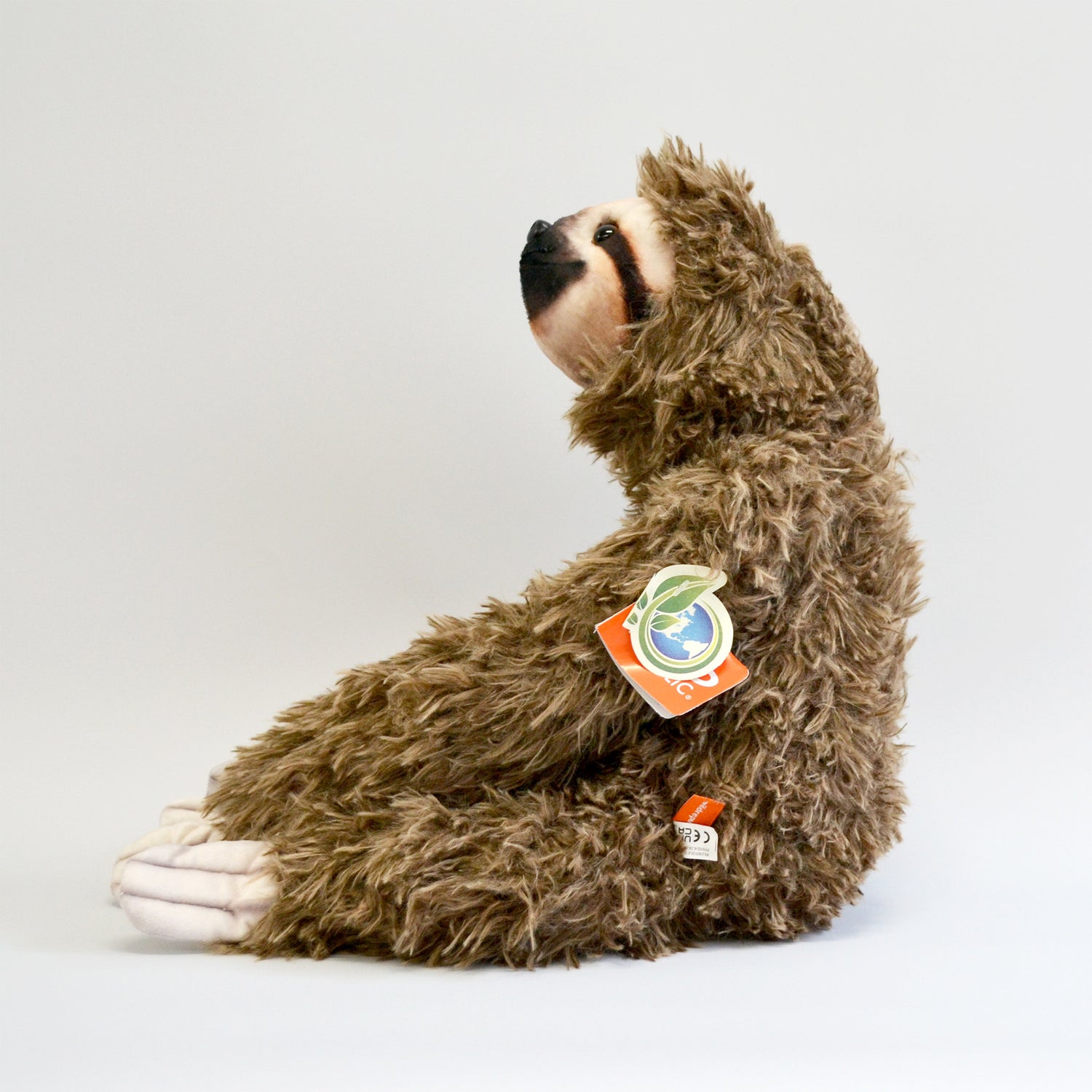 Fluffy sloth plush with long arms, sitting down. Entire body facing the left side