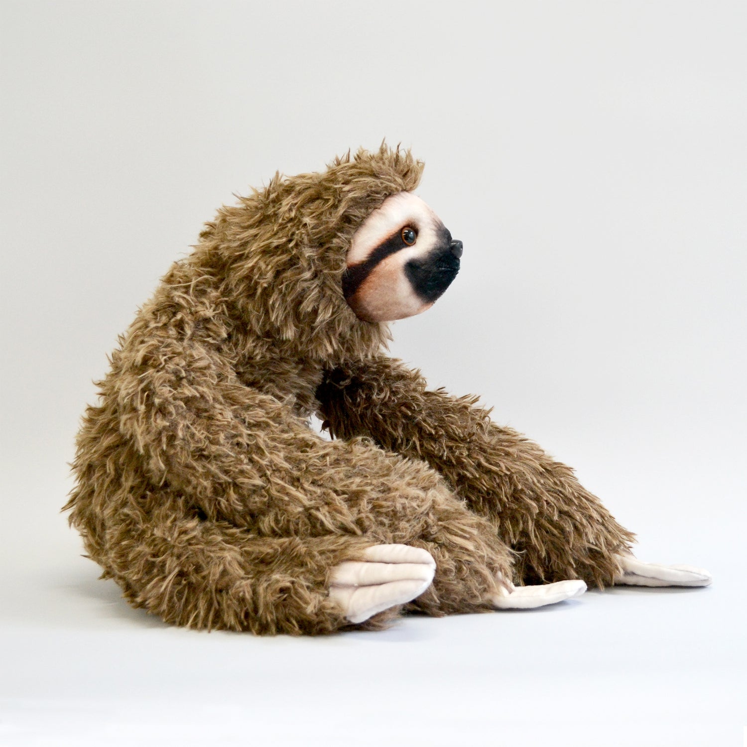 Fluffy sloth plush with long arms, sitting down. Entire body facing the right side