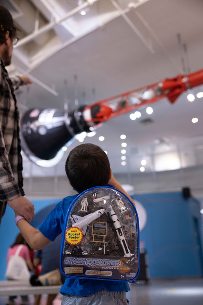 A child and man pointing. The child has a clear and blue space backpack which says SPACE EXPLORER.